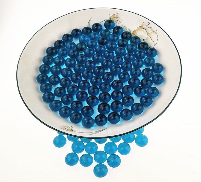 Blue glass marbles on a decorative plate with additional marbles scattered below.