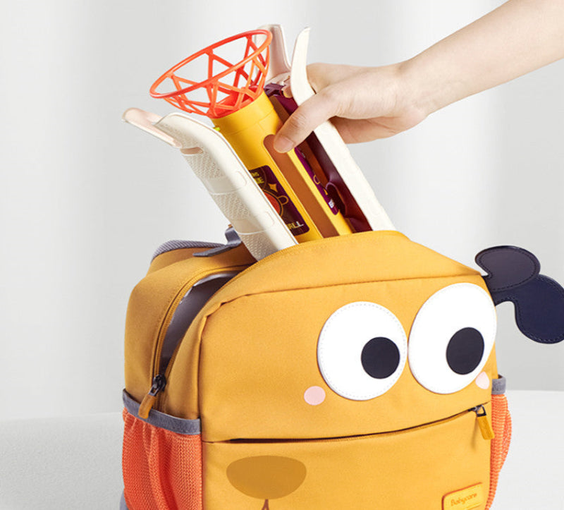 Yellow backpack with cartoon face design, resembling a dog, being used to hold a toy basketball set.
