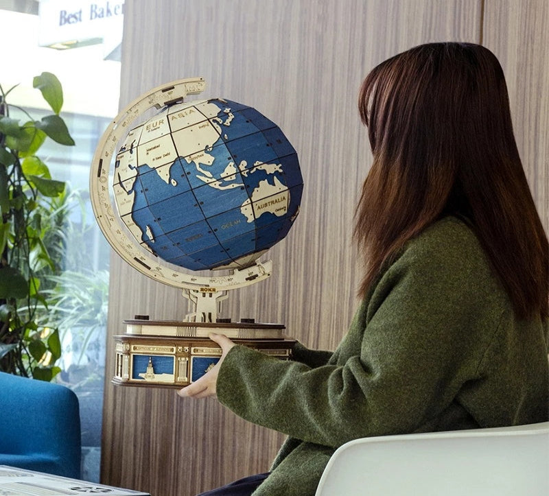 Person holding a decorative globe in an indoor setting with plants and a window.
