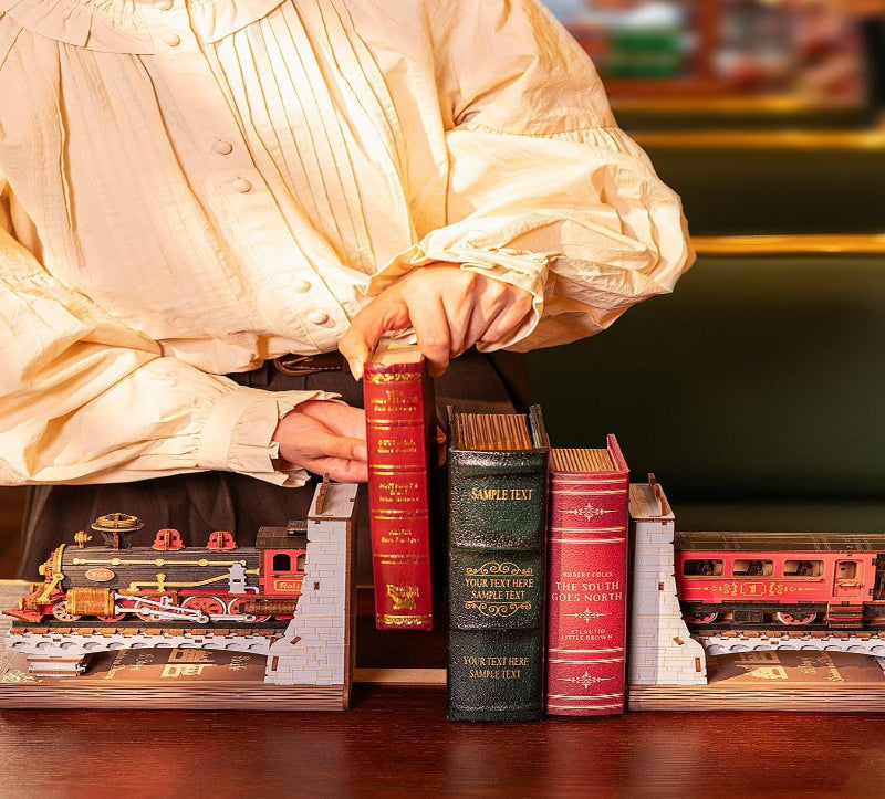 Person holding a stack of books with toy trains on a wooden surface
