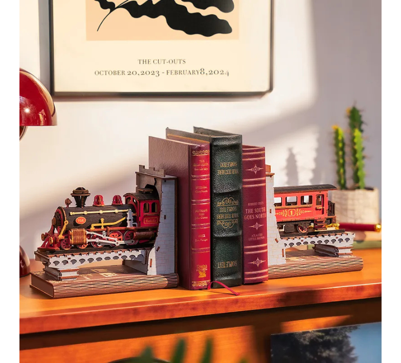 Decorative bookends shaped like a train and books on a wooden surface with a framed picture in the background.