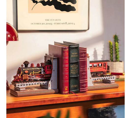 Decorative bookends shaped like a train and books on a wooden surface with a framed picture in the background.