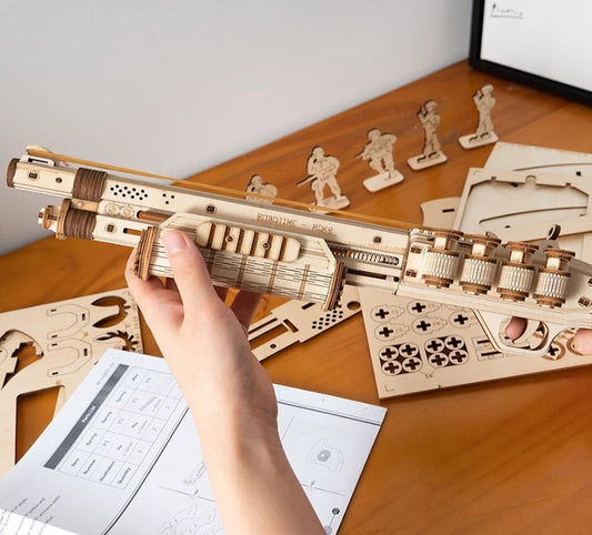 Hand holding a wooden laser-cut model kit on a wooden table with assembly instructions.